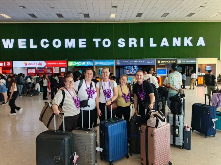 Travellers with their suitcases under the Welcome to Sri Lanka sign at the airport