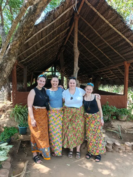 Travellers in colourful sarongs outside a thatched village hut